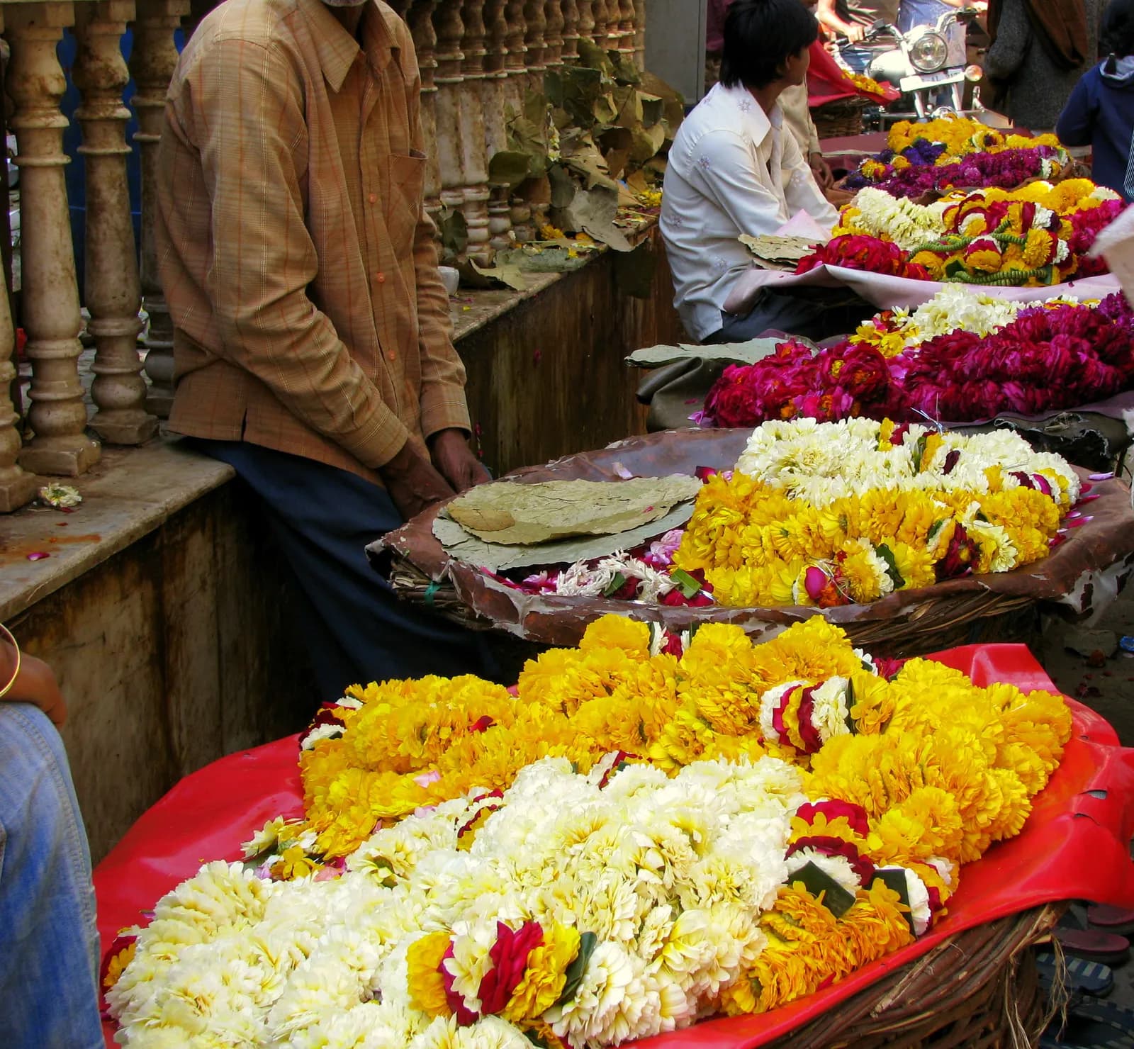 Garland sellers outside the Banke Bihari temple with baskets of marigold, rose and jasmine malas laid out on red cloth