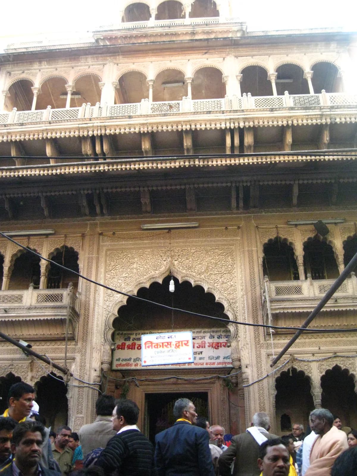 The carved sandstone facade and arched main gate of the Banke Bihari temple in Vrindavan, with devotees crowding the entrance below the Gate No. 1 sign