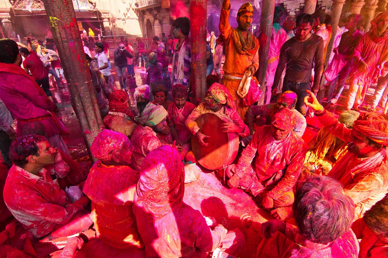 Devotees covered head to foot in pink and red gulal, seated with a drum inside the Barsana temple during Lathmar Holi