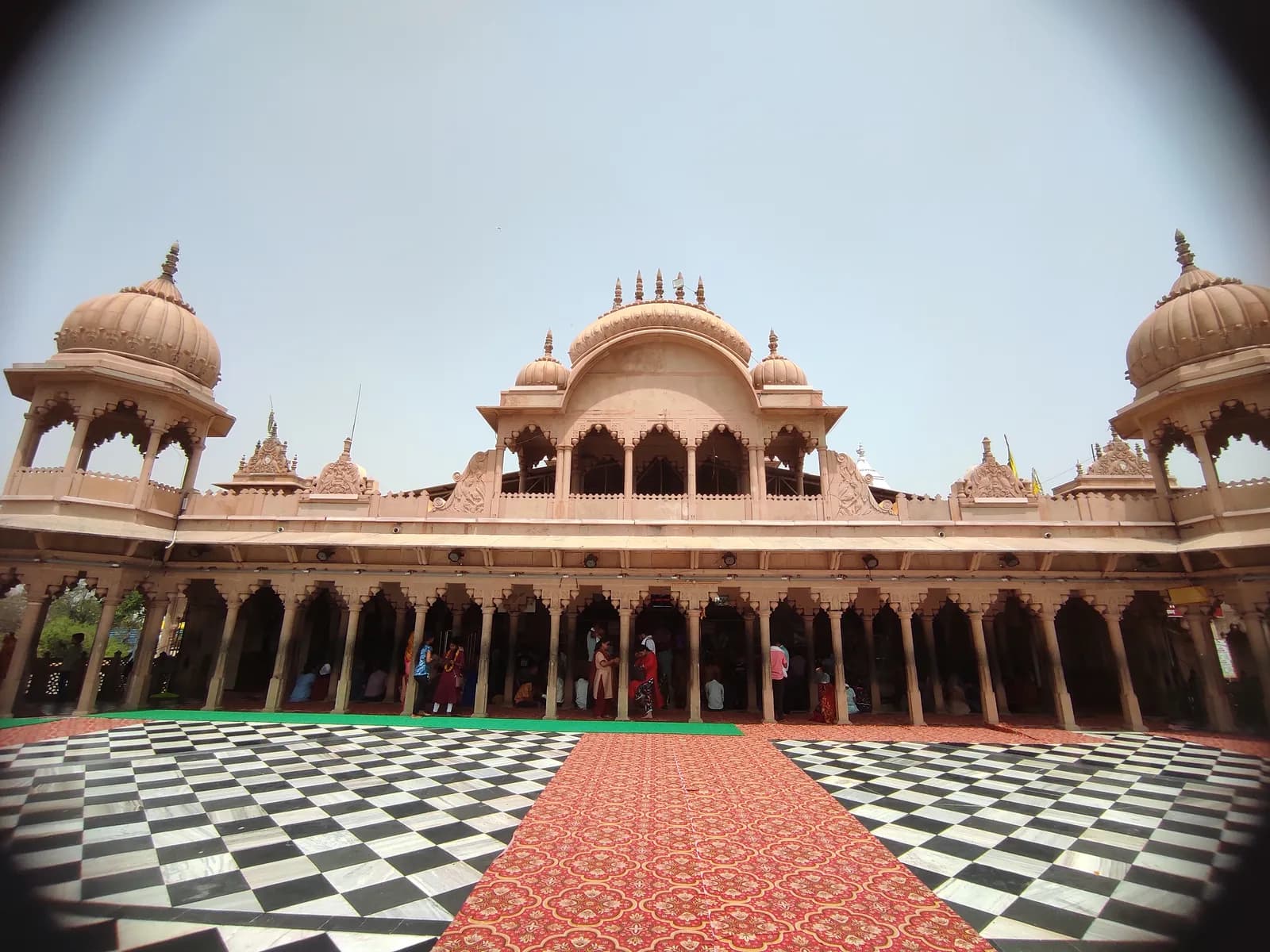 The pink sandstone courtyard of the Shriji temple at Barsana in daylight, its domed chhatris and pillared galleries rising above a chequered marble floor
