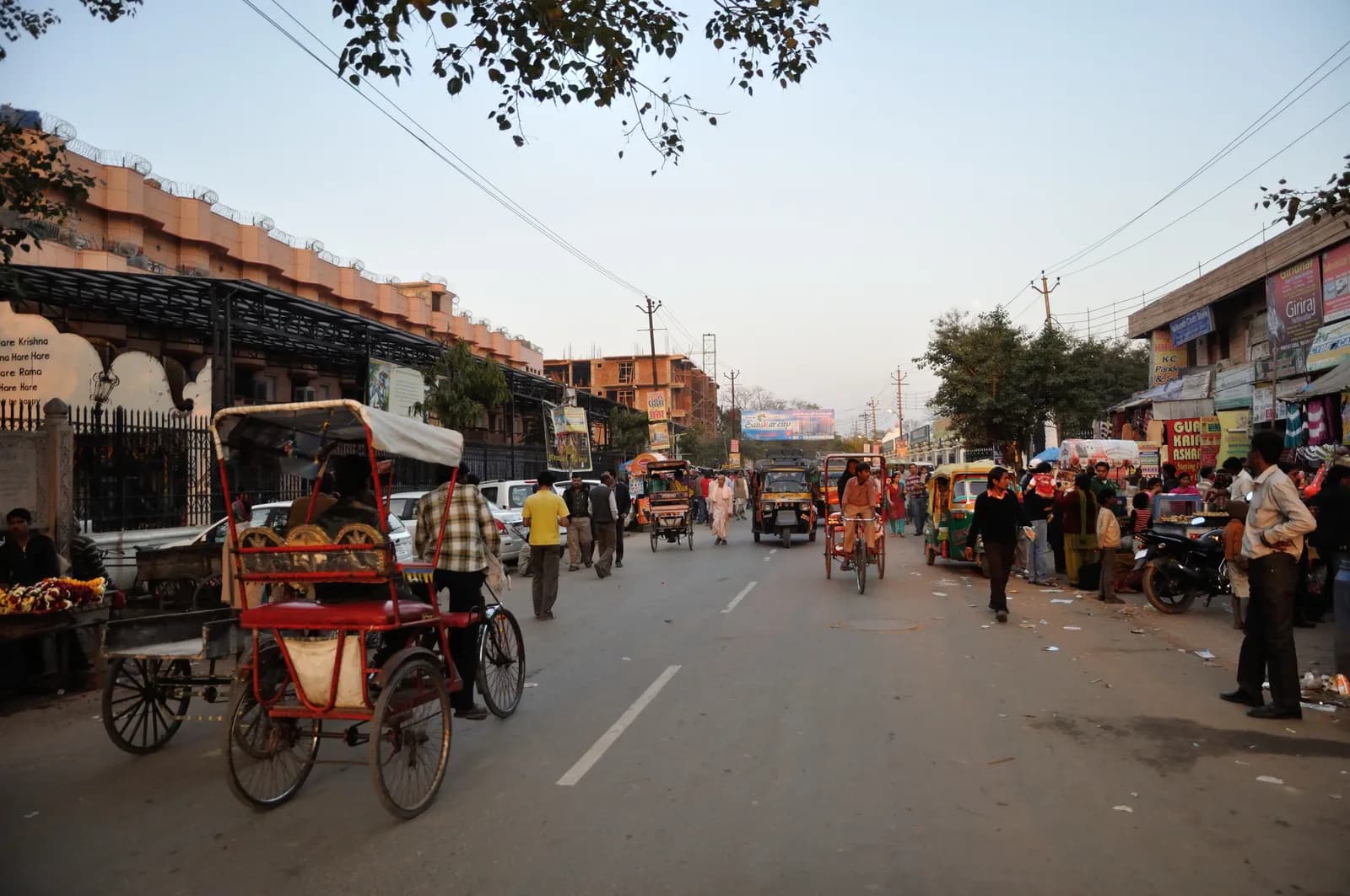 Cycle rickshaws and pilgrims on Bhaktivedanta Swami Marg in Vrindavan, temple walls and shopfronts lining the road